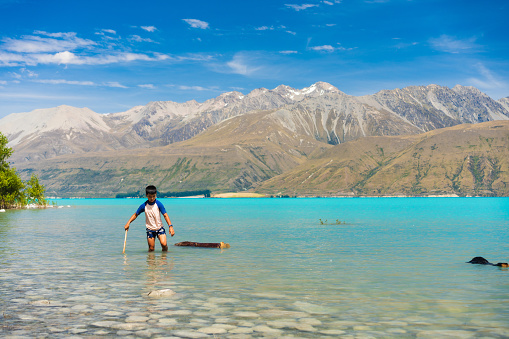 Joyful kids splash in Lake Pukaki's turquoise waters, surrounded by Southern Apls of South Island, New Zealand.