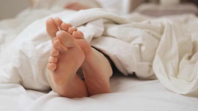 Women's feet itch in bed under a white blanket. Foot diseases, fungus