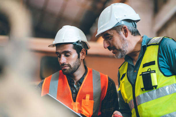 istock Teamwork men in construction site, Two civil engineer or professional foreman in safety helmet hard hat using blueprint in digital tablet working while standing at industrial factory, teamwork concept 1489960339