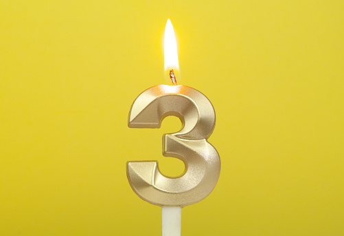 Burning gold birthday candle on yellow background. Number 3.
