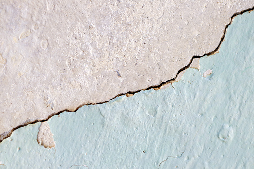 A cracked concrete wall painted in a pastel color.
