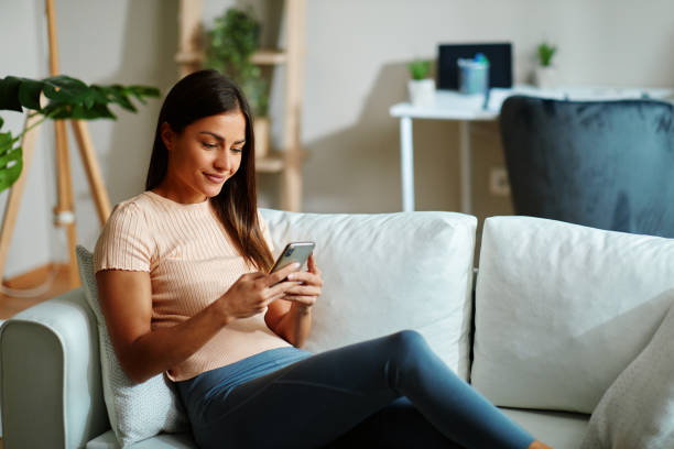 istock Beautiful young woman sitting on sofa and using smartphone 1489971948
