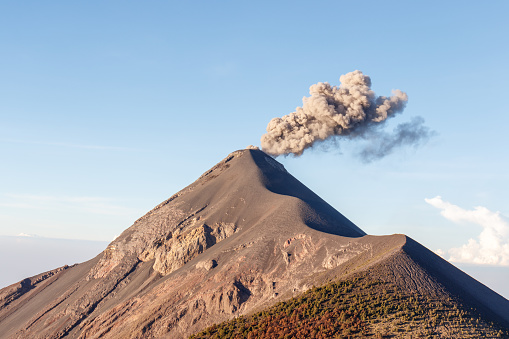 Volcan or volcano Fuego erupting with grey smoke column on a bright, clear day near Antigua, Guatemala, Central America