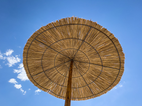 Straw parasol against a blue sky with white clouds. High quality photo