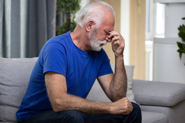 istock Distressed or depressed senior man sitting alone on sofa at home holding his hands by the head. Loneliness concept 1489982379