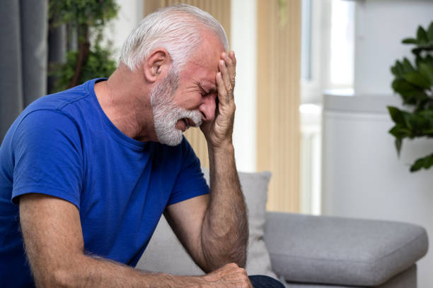 istock Distressed or depressed senior man sitting alone on sofa at home covering his face with hands and crying. Loneliness concept 1489982396