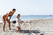 Young happy mother and her little son exercising and having fun with battling rope at a beach gym