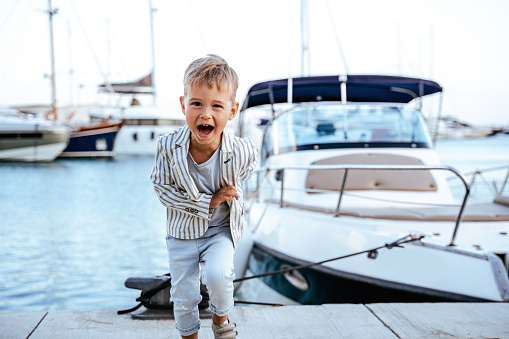 Excited stylish boy running  near yacht in marina.