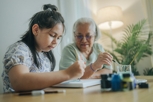 Happy grandmother coloring with her granddaughter at home.