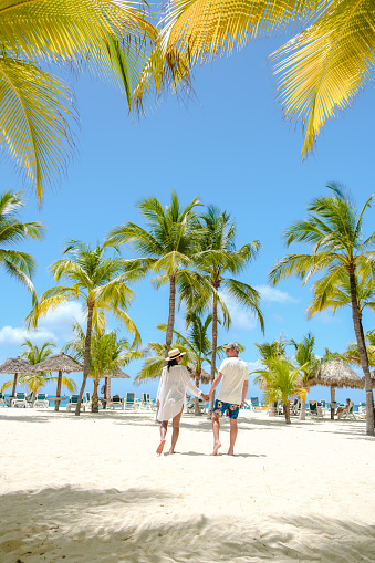 Palm Beach Aruba Caribbean, a couple of men and women at a white long sandy beach with palm trees at Aruba Antilles.