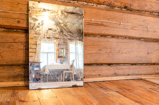 old mirror stands on wooden floor in rural log house (focus on the mirror)