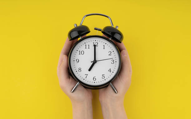 istock Woman's hands holding a black alarm clock on a yellow background 1489992935