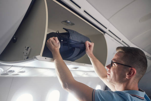 Man travel by airplane Man travel by airplane. Passenger putting hand baggage in lockers above seats of plane. hand luggage stock pictures, royalty-free photos & images