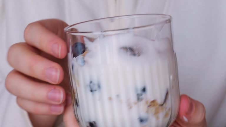 Woman holding Morning granola breakfast with homemade greek yogurt, blueberries in glasses on blue wooden background. Healthy diet Crunchy granola with yogurt nuts and blueberries