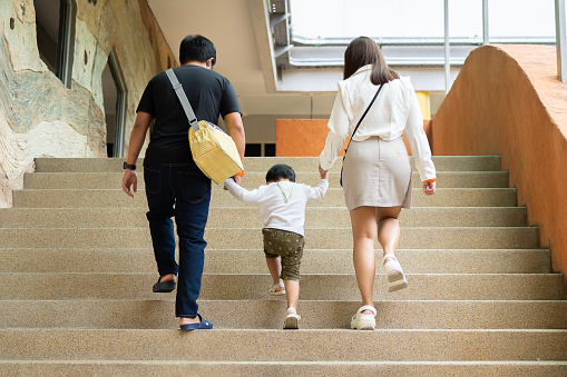 Back view of happy Asian family walking up the stairs. Happy family travel and vacations concept.