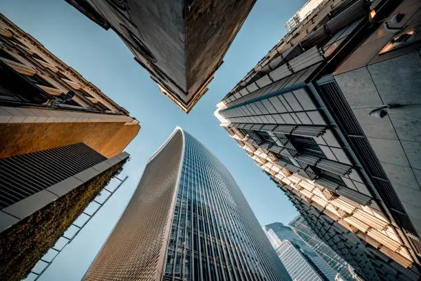 Highly detailed abstract wide angle view up towards the sky in the financial district of London City and its ultra modern contemporary buildings with unique architecture on a clear sky afternoon with sun lit roofs of the tallest structures. Photographed from the base of the Walkie-Talkie building at 20 Fenchurch street. Shot on Canon EOS R5 full frame with 10mm prime wide angle lens. Image is ideal for background with many concepts.