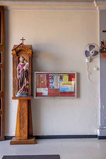 St. Sylvester's Church, Negombo, Western Province, Sri Lanka - March 9th 2023:  Figure of a male saint beside a bulletin board and a ventilator close to the entrance
