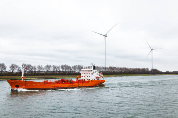 A tanker ship passing through a canal in the Netherlands with wind generators on the shore.