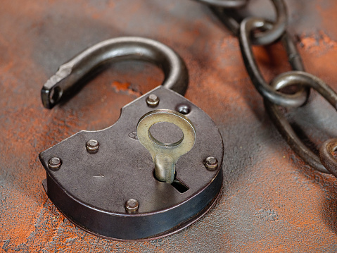 Open padlock with key and an old rusty link chain on a grunge orange background
