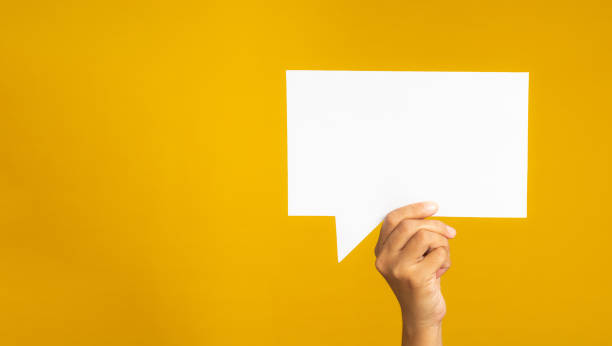 istock Hand holding of an empty white speech bubble against a yellow background 1490031902