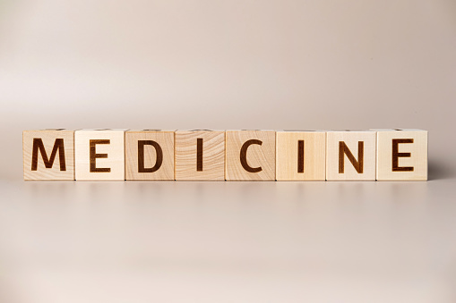 The word MEDICINE on wooden cubes on a beige neutral studio background. Copy Space. Written. Text words matter. Supplements for human health. Essential nutrient vitamins, mineral. Medical Concept.
