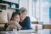 happy chinese grandmother hugging her granddaughter in living room
