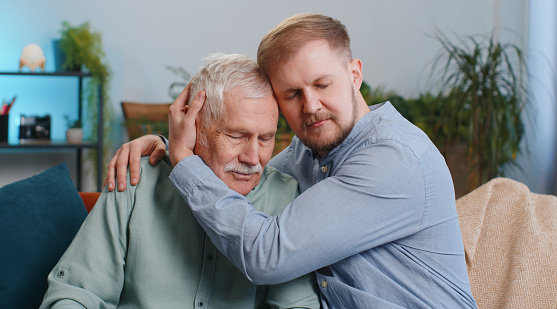 Adult man grandson supporting, giving psychological help to senior grandfather. Health problems, crisis, bankruptcy, impotence. Compassion. Son asking for apologizes to offended stressed elderly daddy