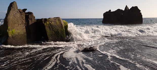 You see a beautiful ocean scenary on the famous beach Praia Formosa in Funchal Madeira. There are shown a blue sky, gently waves and great spray of the atlantic ocean.