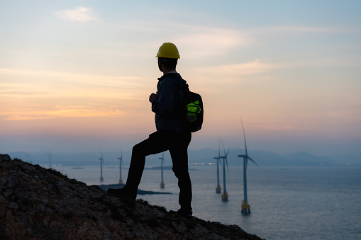 Climbers stop on the side of the mountain to enjoy the sunset view of the seaside wind farm