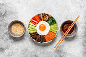 Traditional Korean dish Bibimbap. Rice with beef, vegetables, mushrooms and fried egg in a bowl. View from above. Light grunge background.