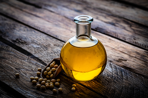 Close up view of a glass bottle filled with soy oil shot on rustic wooden table. Some dried soybeand complete the composition Plant-based nutrition concept. High resolution 42Mp studio digital capture taken with Sony A7rII and Sony FE 90mm f2.8 macro G OSS lens