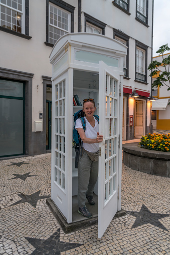 A mature women, tourist, coming out of old telephone booth. Ponta Delgada City Hall, Azores