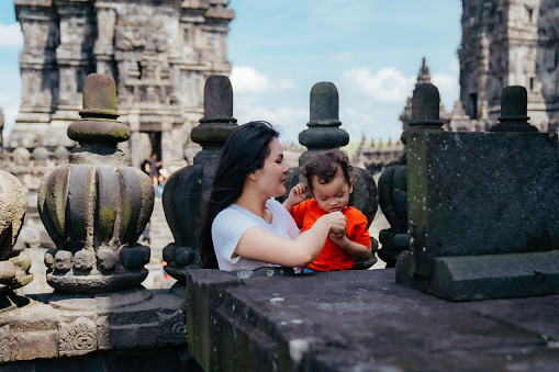 asian woman carrying her son visiting prambanan temple, Yogyakarta