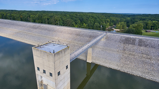 Image of Aerial of a concrete dam with gravel slopes and crows on the rood and on the bride and a forest in the background