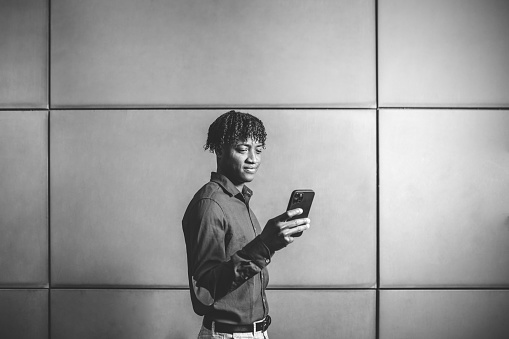 Professional African American smiling in the financial district with his mobile. Monochrome version. Photograph of an African American man holding a smartphone in the city. Monochrome version.