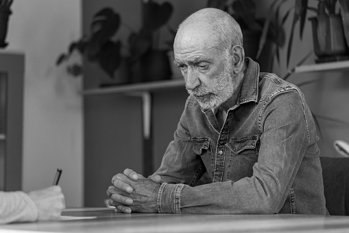 Black and white photo of a depressed man having psychotherapy in his cozy home.