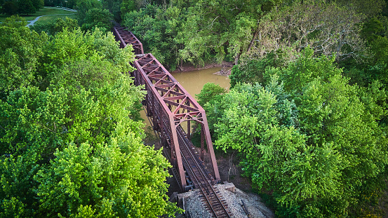 Image of Aerial view above large metal bridge for train tracks over river surrounded by green trees