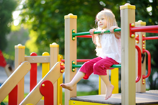Cute little girl having fun on a playground outdoors in summer. Sport activities for kids.