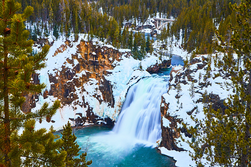 Image of Amazing blue and peaceful waterfall by snowy cliffs and pine trees in Yellowstone