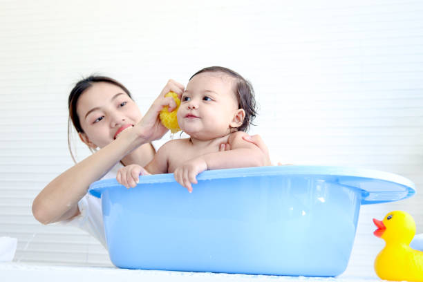 Happy toddle baby infant has fun while taking bubble bath in bathroom, mother bathing kid in tub, mom washing and cleaning her little toddler girl daughter child in bath, childhood and parent care.