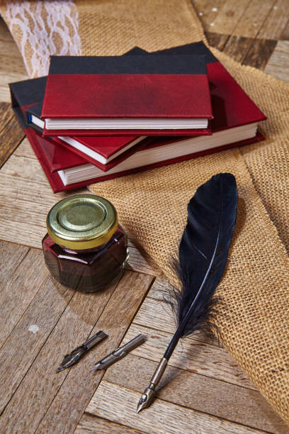 istock Black feather quill with additional nibs lays next to a closed ink pot and three red and black journals 1490080241