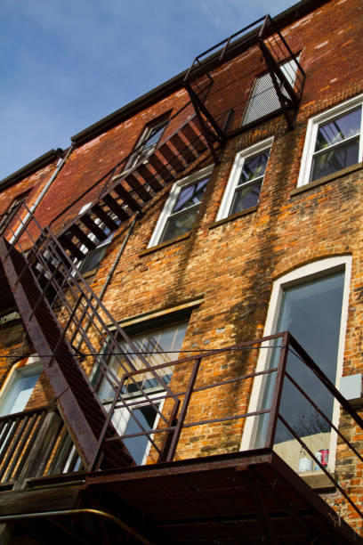 istock Black fire escape steps climb a brick building with many windows 1490080244