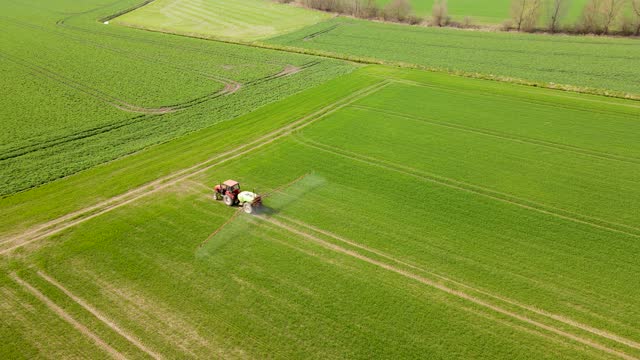 Tractor with farmer spraying wheat crop growing in hilly agricultural field