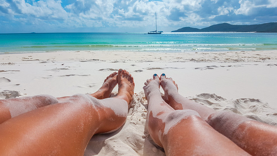 A blissful summer vacation on beautiful Whitehaven Beach toes in the sand and eyes on the horizon as clouds sail across a clear sky in Queensland, Australia.