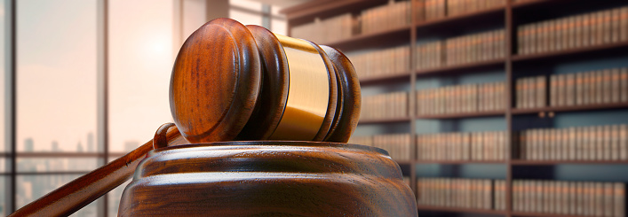A gavel rests in front of a bookshelf of law books out of focus in the background.