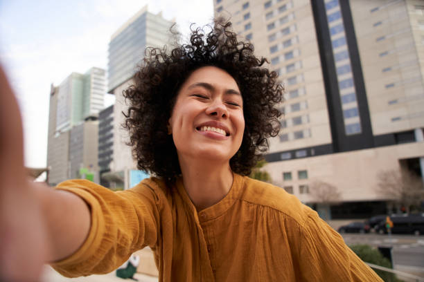 portrait d’une jeune américaine souriante les yeux fermés et afro prenant un selfie à l’extérieur d’un centre commercial - close up human eye photography color image photos et images de collection