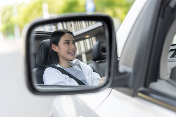 車の中で笑顔でサイドミラーを見る美しい若い女性 - owner women car rear view mirror ストックフォトと画像