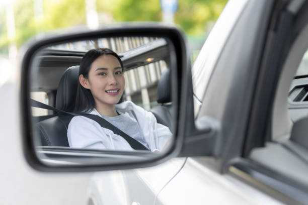 車の中で笑顔でサイドミラーを見る美しい若い女性 - owner women car rear view mirror ストックフォトと画像