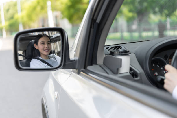 車の中で笑顔でサイドミラーを見る美しい若い女性 - owner women car rear view mirror ストックフォトと画像