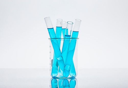 Detail of a colorful test tubes inside a beaker, over a white background.